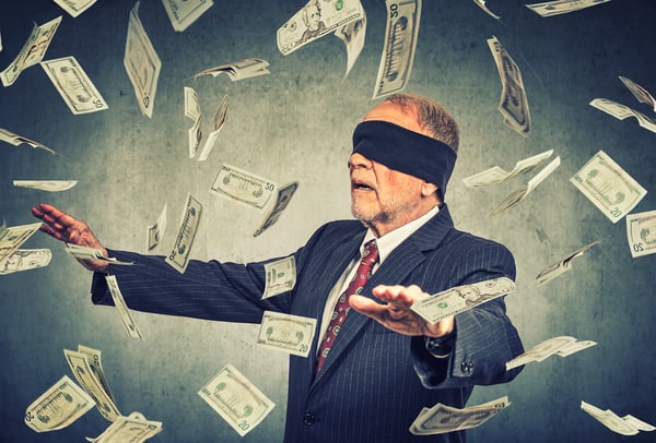 Blindfolded senior businessman trying to catch dollar bills banknotes flying in the air on gray wall background. Financial corporate success or crisis challenge concept