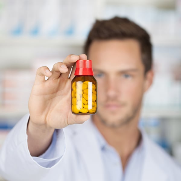 Closeup of a blurred male pharmacist holding out tablets in bottle at drugstore