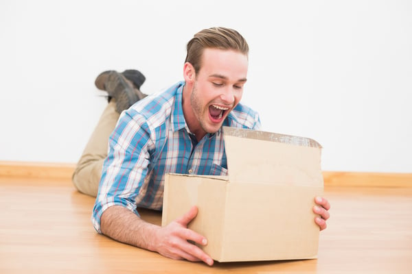 Surprised man lying on the floor opening boxe at home in the living room