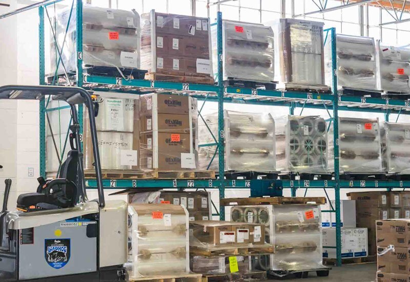 Pallets of stretch film and packaging materials stored on warehouse racking with a forklift in the aisle at Industrial Packaging