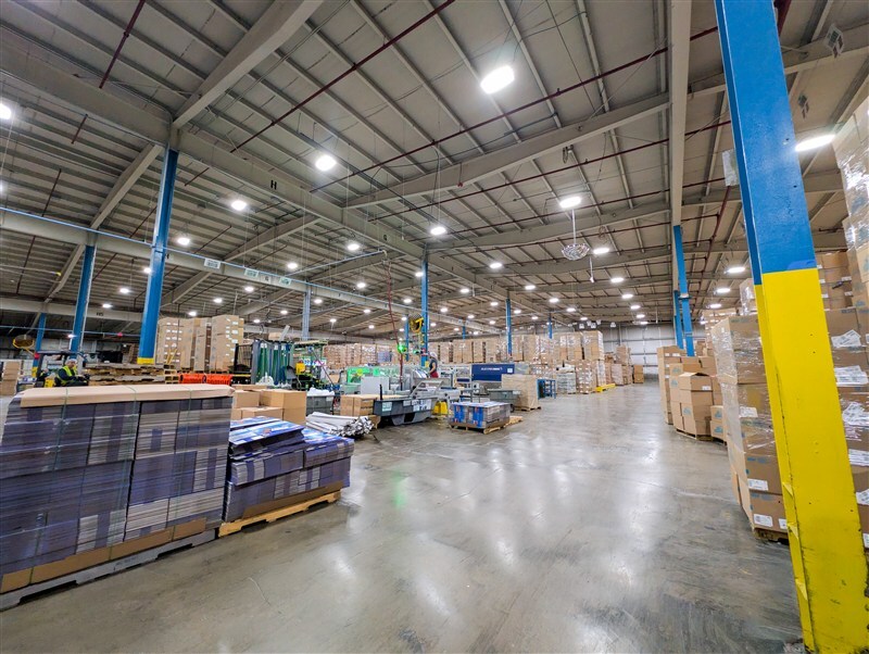 Forklift operator moving pallets of finished club packs in organized warehouse section with clear aisle markings
